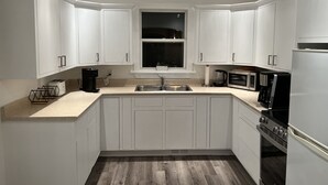 Eine moderne Küche mit weißen Schränken, einer Edelstahl-Spüle, einer Kaffeemaschine, einer Mikrowelle und einem Backofen.
