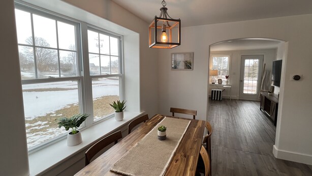 Ein Essbereich mit Holztisch und Stühlen, einer hängenden Leuchte und Blick auf verschneite Landschaft durch große Fenster.