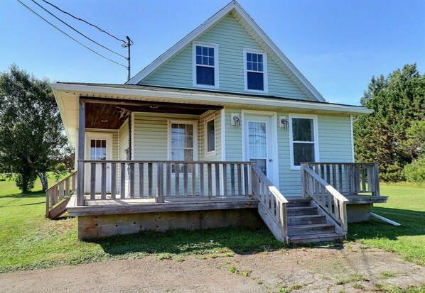 A two-story house with a front porch, a small front yard, and a wooden staircase leading to the entrance. - Cricker's Corner Vacation Home - North Rustico (North Rustico)