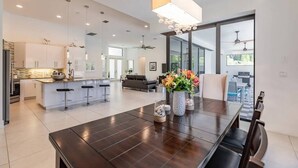 A spacious kitchen with a central island, a dining area with a dark wooden table, and large windows offering a view of the outdoors. - Villa Aviator (Cape Coral)