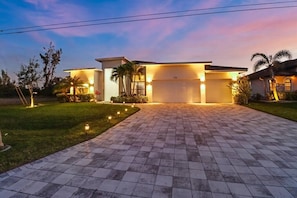 A modern house with a paved driveway, garage, and well-lit exterior.