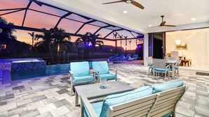 A spacious outdoor lounge area with seating and a pool, featuring a glass ceiling and palm trees in the background. - Villa Aviator (Cape Coral)