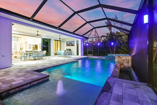 An indoor swimming pool with a glass ceiling, a patio area with chairs, and a view of the outdoors.