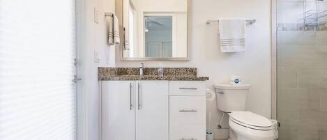 A modern bathroom with a white vanity, a toilet, and a shower area.