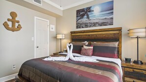 Hotelkamer met een bed, nachtkastje, lamp, schilderij van een strandgezicht en een wandbeugel.