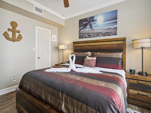 A hotel room with a bed, a nightstand, a lamp, a painting of a beach scene, and a wall anchor. - Dawn 223 - Buena Vista by Ryson Vacation Rentals (Galveston)