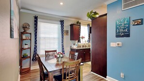 Een eetgedeelte met een houten tafel en stoelen, een keuken met donkere kastjes, en een blauwe accentmuur met een bord met strandthema.