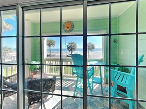 A balcony with turquoise chairs and a wicker chair, overlooking a beach with palm trees and a clear sky. - Dawn 223 - Buena Vista by Ryson Vacation Rentals (Galveston)