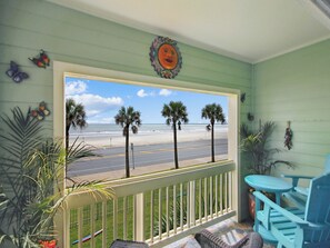 A balcony with a view of the beach, palm trees, and a blue chair.