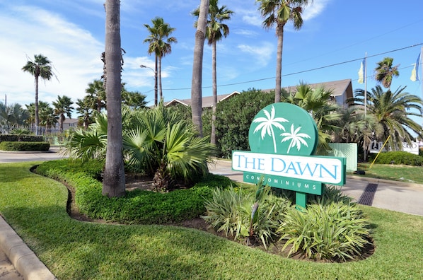 Schild für The Dawn Condominiums mit Palmen und einem gepflegten Rasen.