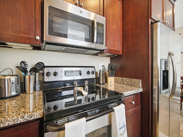 A kitchen with a stainless steel stove, microwave, and refrigerator, wooden cabinets, and granite countertops.