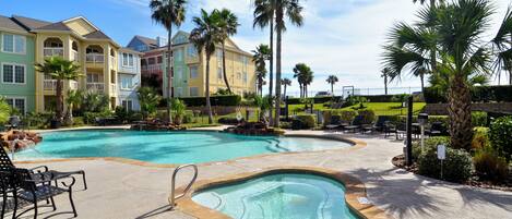 A swimming pool area with multiple pools, lounge chairs, and palm trees.