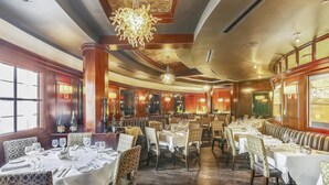 Un vaste espace dédié à la salle à manger, comprenant plusieurs tables et chaises, de grandes fenêtres et des luminaires décoratifs.
