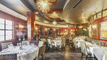 Un comedor amplio con varias mesas y sillas, ventanas grandes y luminarias decorativas.