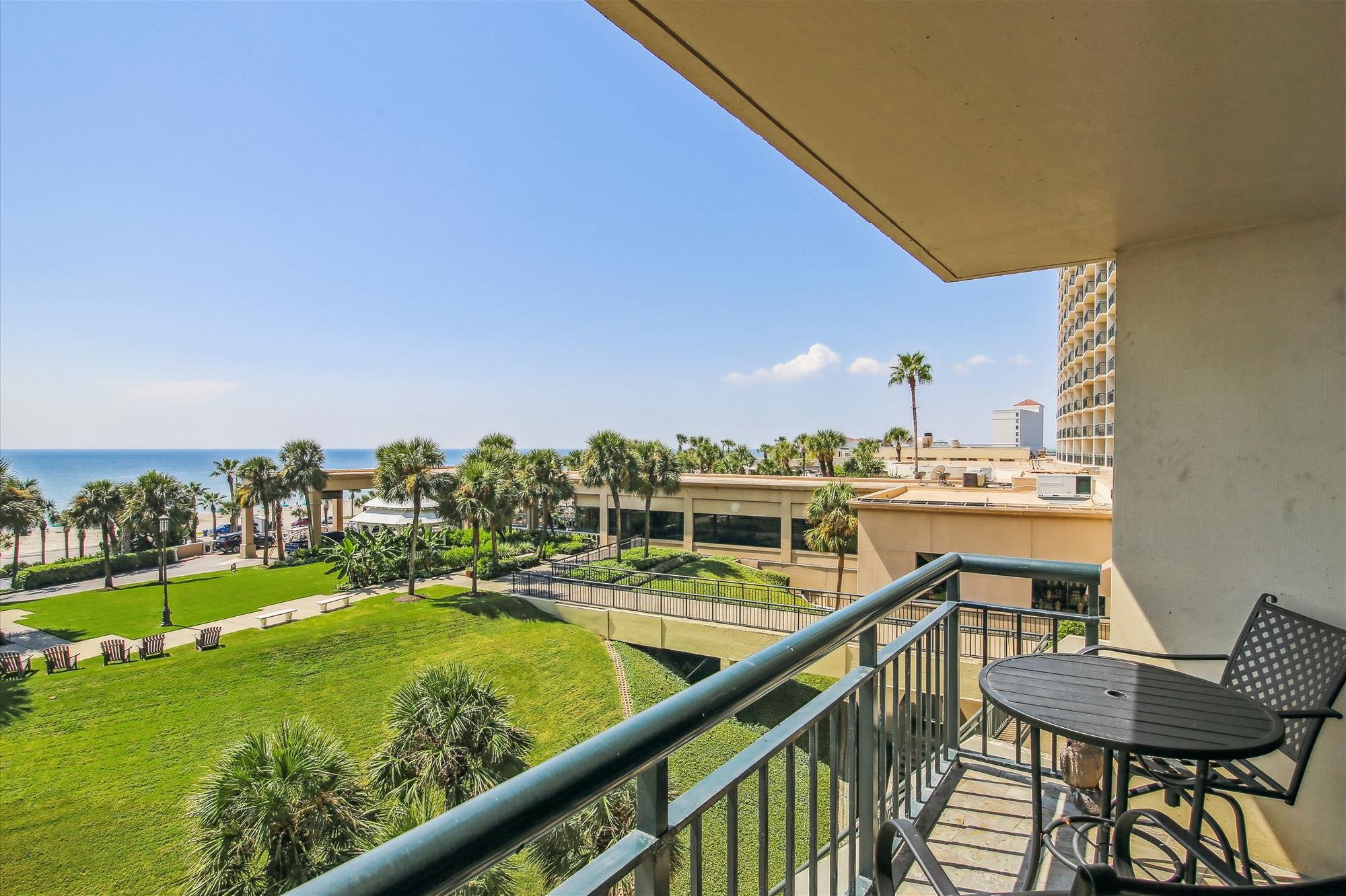 A balcony with a view of the ocean, a grassy area, and a building with a balcony.