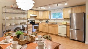 A modern kitchen with wooden cabinets, stainless steel appliances, and a dining area with a table set for two. - Short Walk to Long Pond Swimming Beach! (Wellfleet)