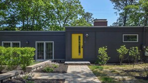 A modern house with a yellow door, a brick chimney, and a paved walkway leading to the entrance. - Short Walk to Long Pond Swimming Beach! (Wellfleet)