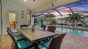 Un espace repas aménagé au bord de la piscine, avec une table et des chaises, un ventilateur de plafond et une vue sur la piscine et les environs.
