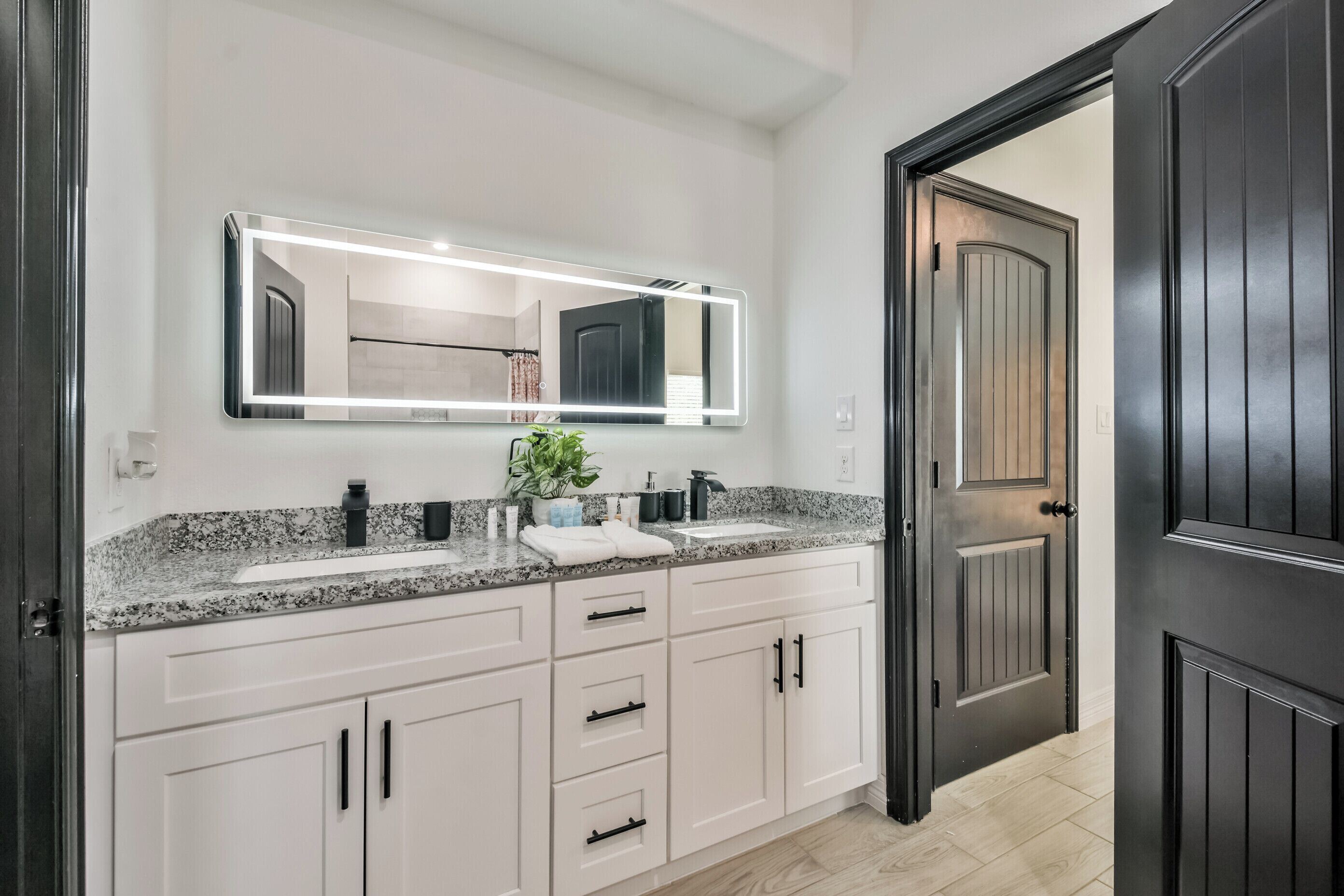 A modern bathroom with a large mirror, two sinks, and a dark door.