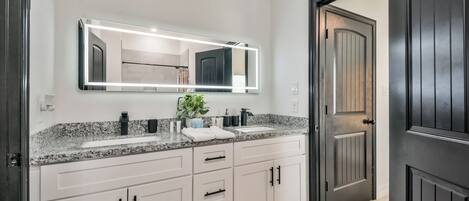A modern bathroom with a large mirror, two sinks, and a dark door.