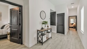 Un couloir avec un plancher en bois, une console avec des rangements, une plante en pot et, au fond, un lit avec des oreillers.