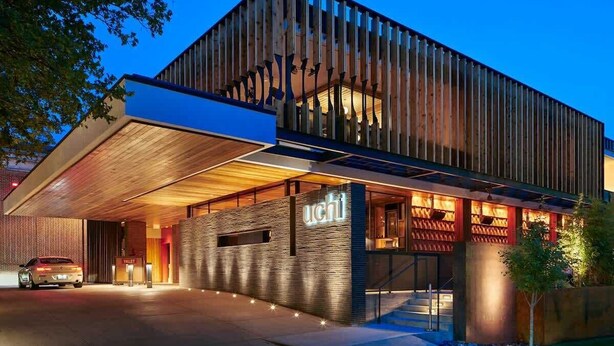 A modern hotel with a prominent 'UCHI' sign, a covered entrance, and a car parked outside. - Mr. Nomad: Parisian PopHouse in Uptown (Dallas)