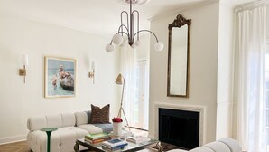 A living room with a sofa, armchairs, a coffee table, a fireplace, a large mirror, and a chandelier. - Mr. Nomad: Parisian PopHouse in Uptown (Dallas)