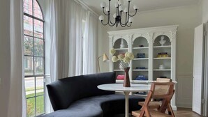 A modern living room with a black sectional sofa, a round white table, and a wooden chair. A white bookshelf with decorative items is in the background. - Mr. Nomad: Parisian PopHouse in Uptown (Dallas)