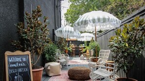 An outdoor patio area with wicker chairs, a chalkboard sign, and potted plants. - Mr. Nomad: Parisian PopHouse in Uptown (Dallas)