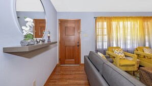 A living room with a wooden door, a mirror, a shelf with decorative items, a sofa, and yellow armchairs. - Nice and modern decor, 4BR 3BA, remodeled (Hagerstown)