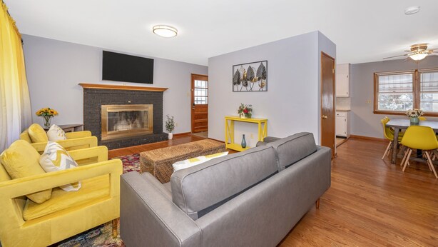 A living room with a fireplace, yellow and gray sofas, a dining area with yellow chairs, and a ceiling fan. - Nice and modern decor, 4BR 3BA, remodeled (Hagerstown)