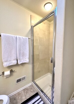 A bathroom with a glass-enclosed shower, two white towels hanging on a rack, a toilet, and a vent.