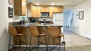 A kitchen with wooden cabinets, a granite countertop, and three bar stools. - Modern, cozy home in private beach community Admirals Cove (Coupeville)