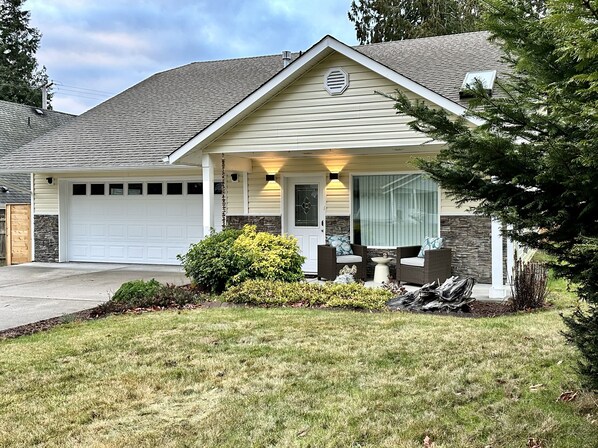 A single-story house with a garage, a covered porch with outdoor seating, and a well-maintained lawn.