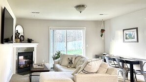 A living room with a sofa, a fireplace, a dining table, and a large window. - Modern, cozy home in private beach community Admirals Cove (Coupeville)