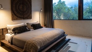 A modern bedroom with a large bed, a view of trees through a window, and a unique wall art piece. - Unho Tulum (Tulum)