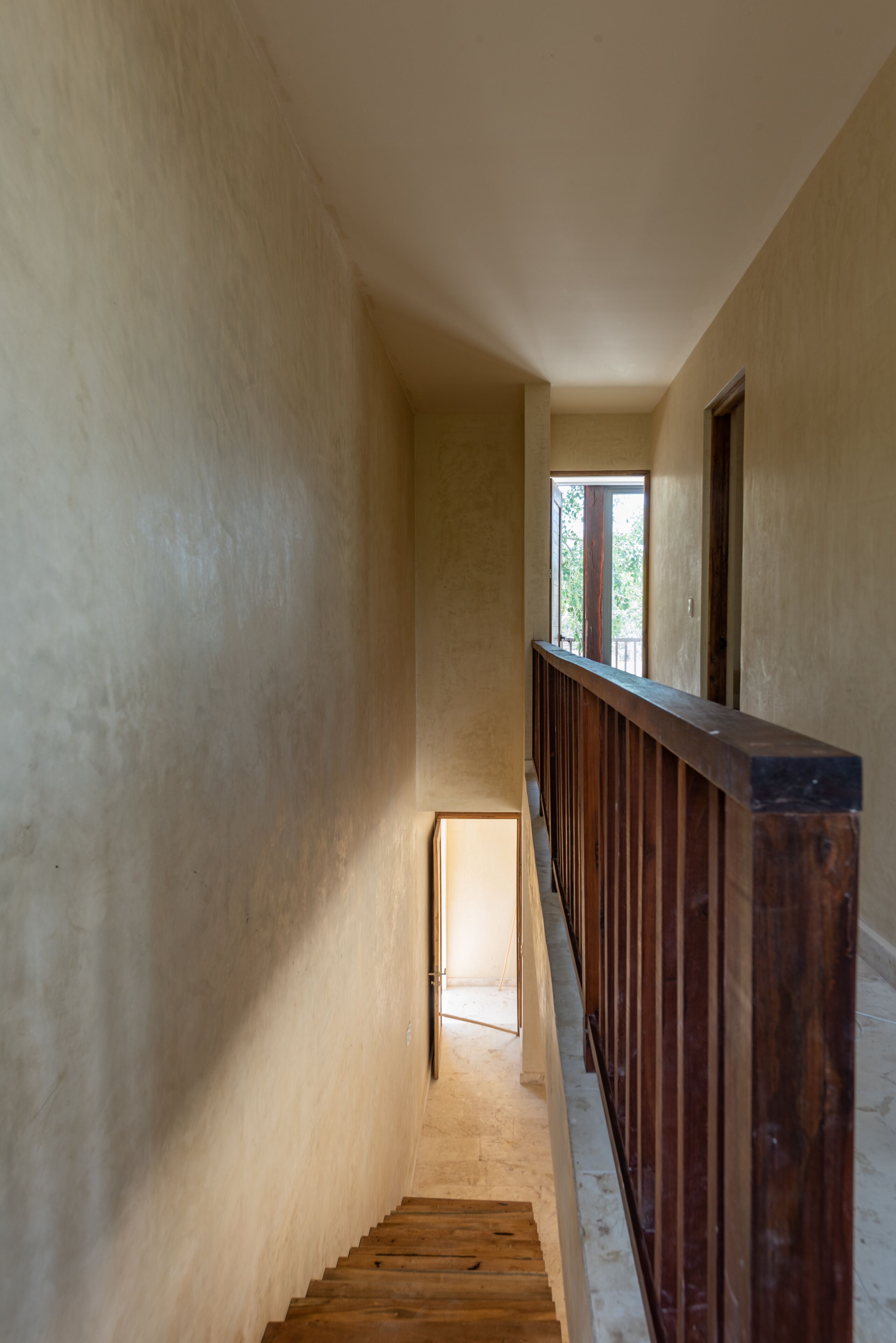 A narrow, dimly lit stairwell with wooden railings and a small window at the top.