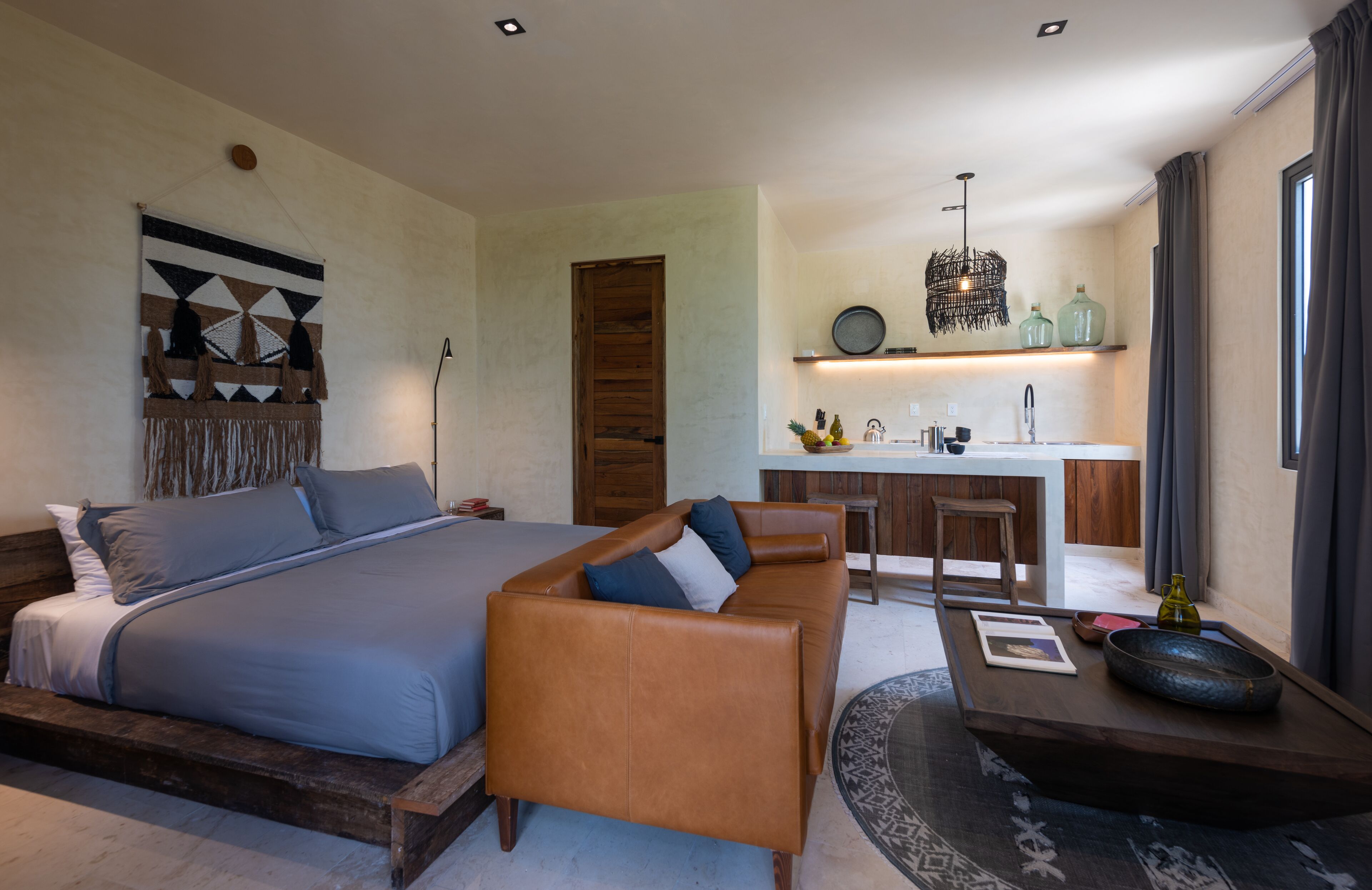A modern bedroom with a large bed, a wooden bench, and a small table with a bowl.