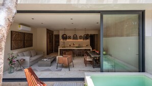 A modern living area with a sofa, chairs, a dining table, and a kitchen area with pendant lights. - Unho Tulum (Tulum)
