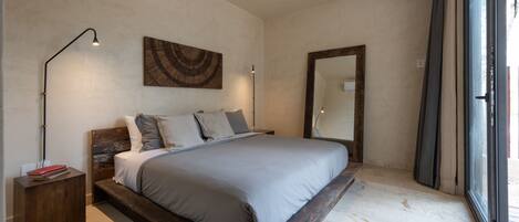 A modern bedroom with a large bed, a bedside table, a floor lamp, a wall-mounted artwork, and a large mirror.