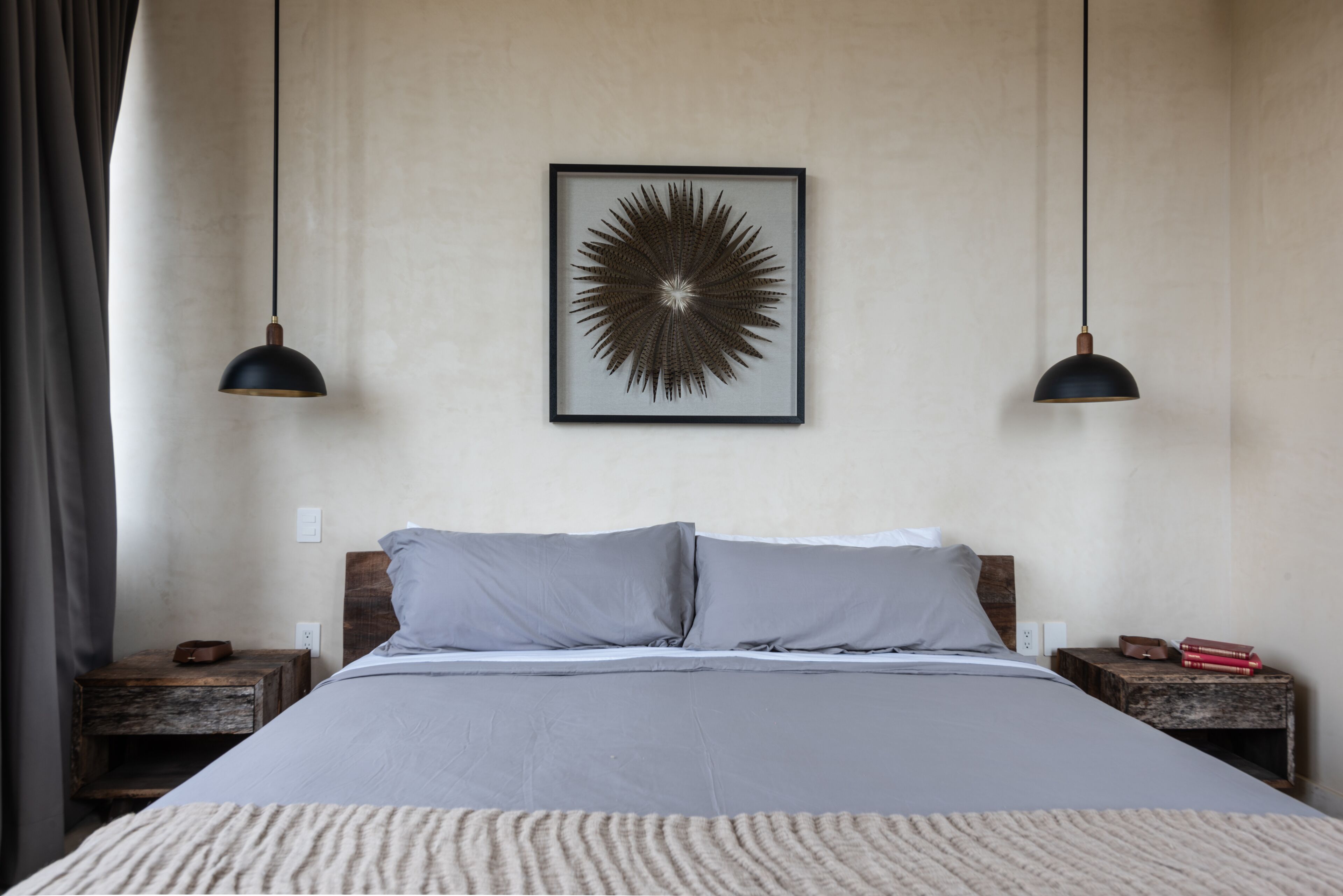 A bedroom with a bed, two nightstands, a framed artwork, and two pendant lights.