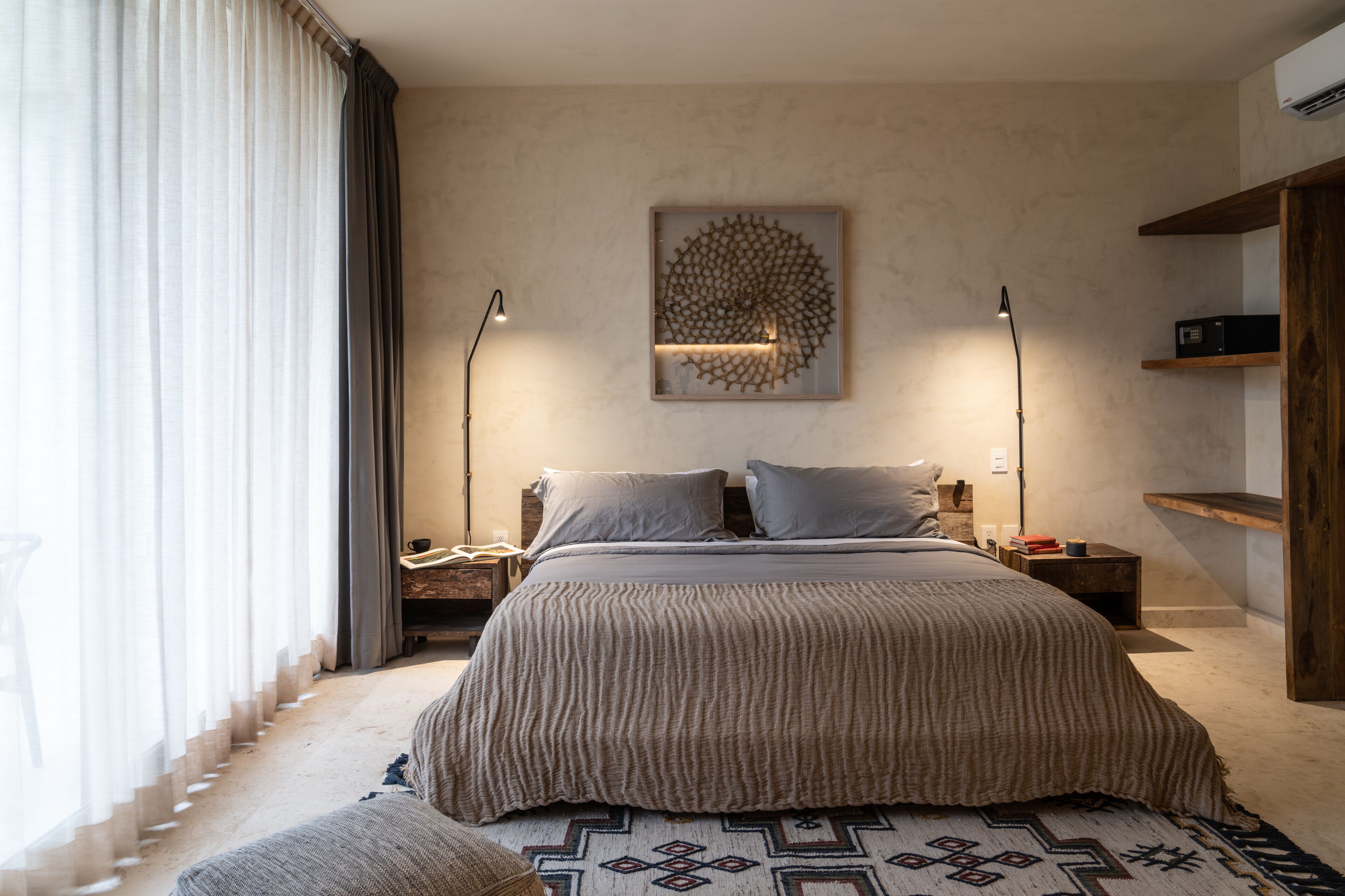 A modern bedroom with a large bed, two bedside lamps, a geometric wall art piece, and a wooden shelf.