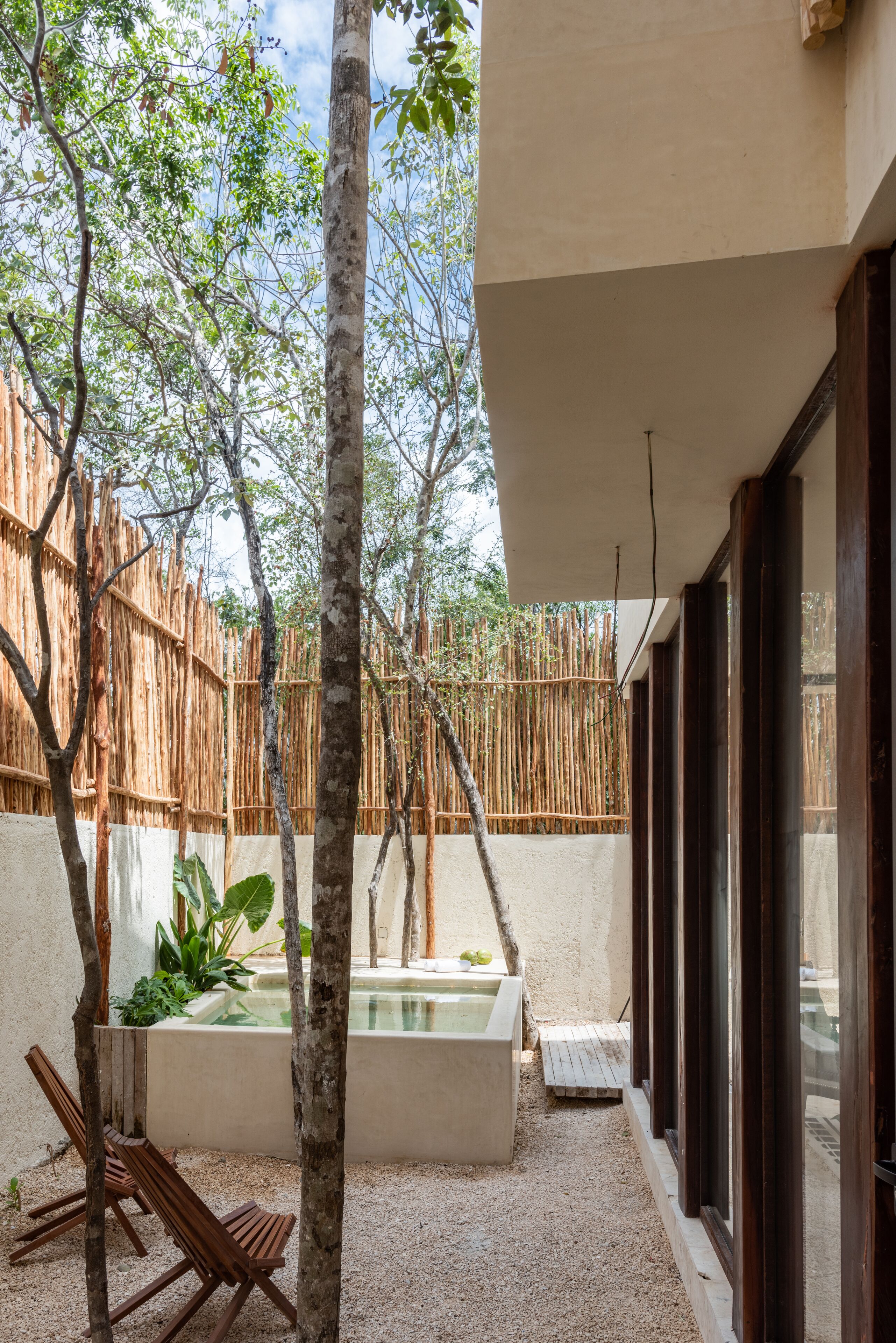 Un espace extérieur moderne doté d’une piscine, de chaises en bois et d’une clôture en bambou.