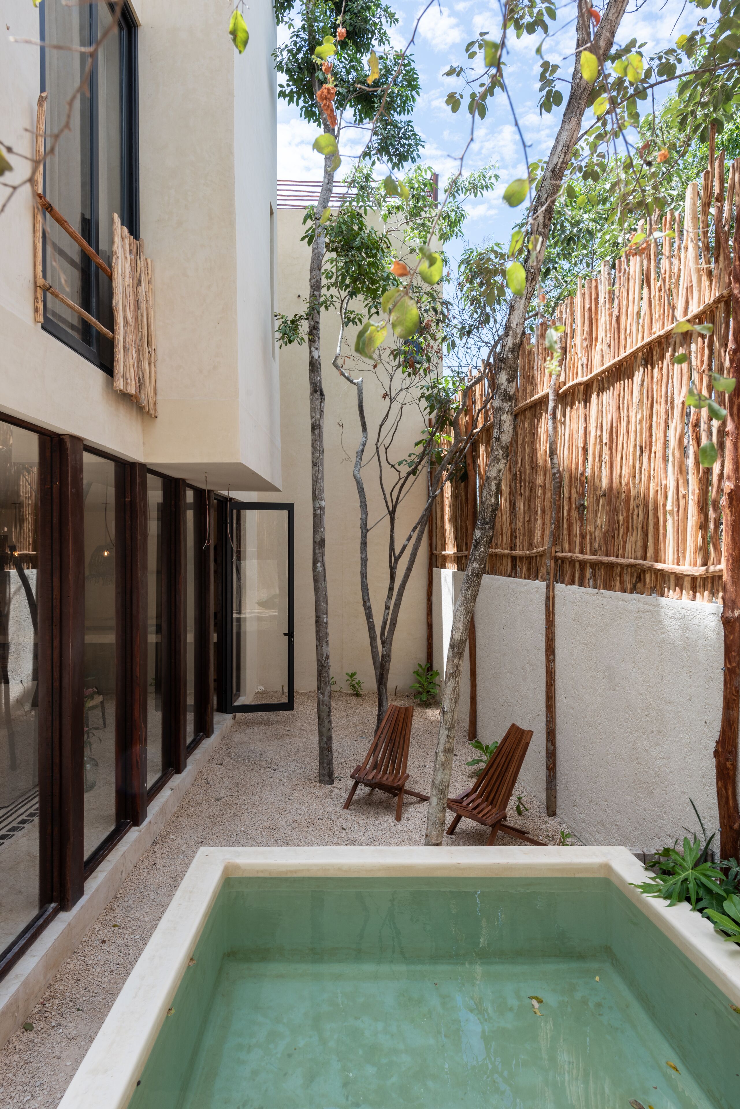 A courtyard with a swimming pool, wooden chairs, and a bamboo fence.
