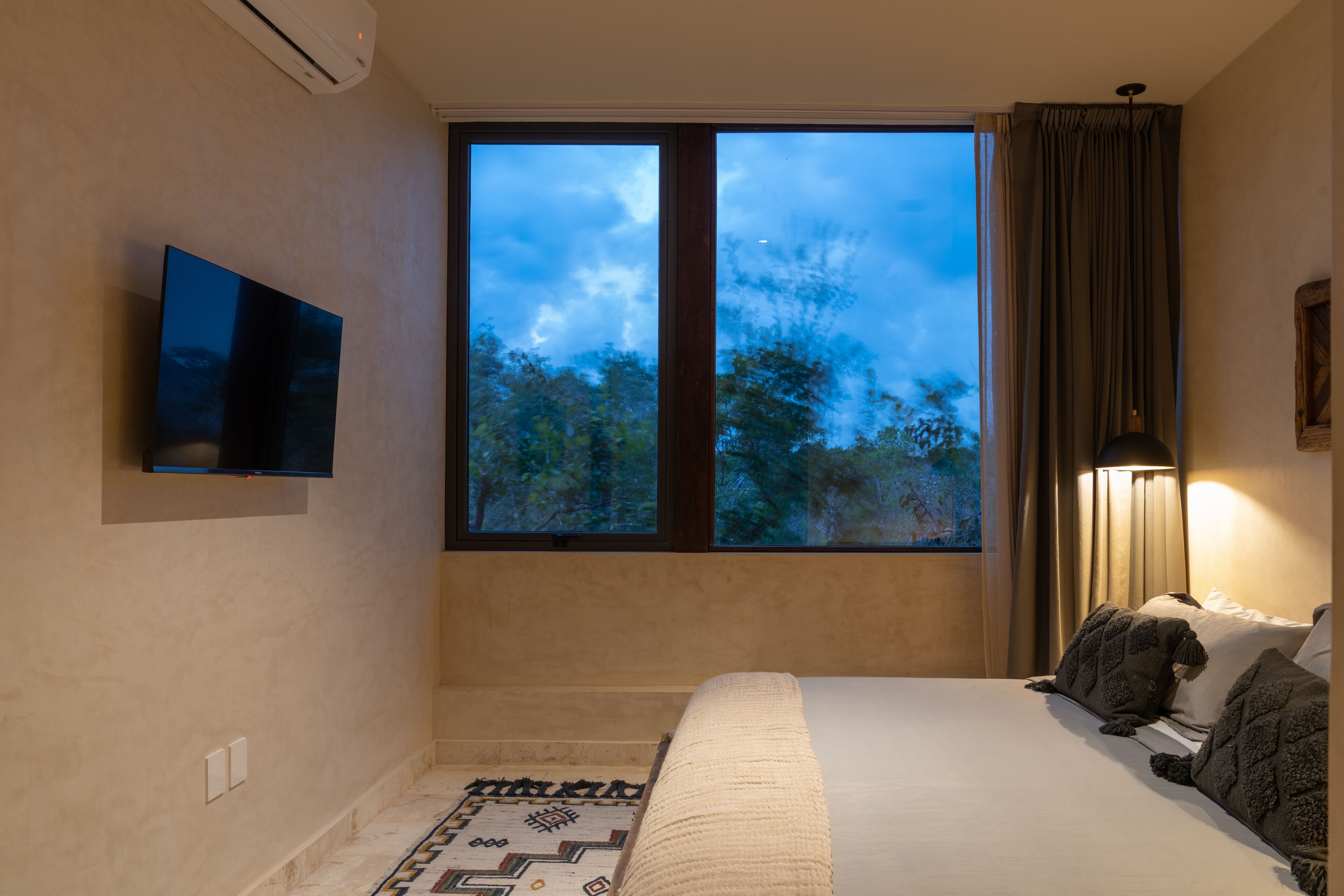 Una camera da letto con un letto, una TV a parete, una finestra con tende e un tappeto decorato.