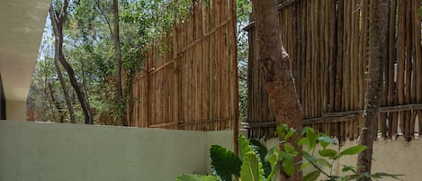 A wooden bench, a small table, and a hot tub in a shaded outdoor area with a bamboo fence.