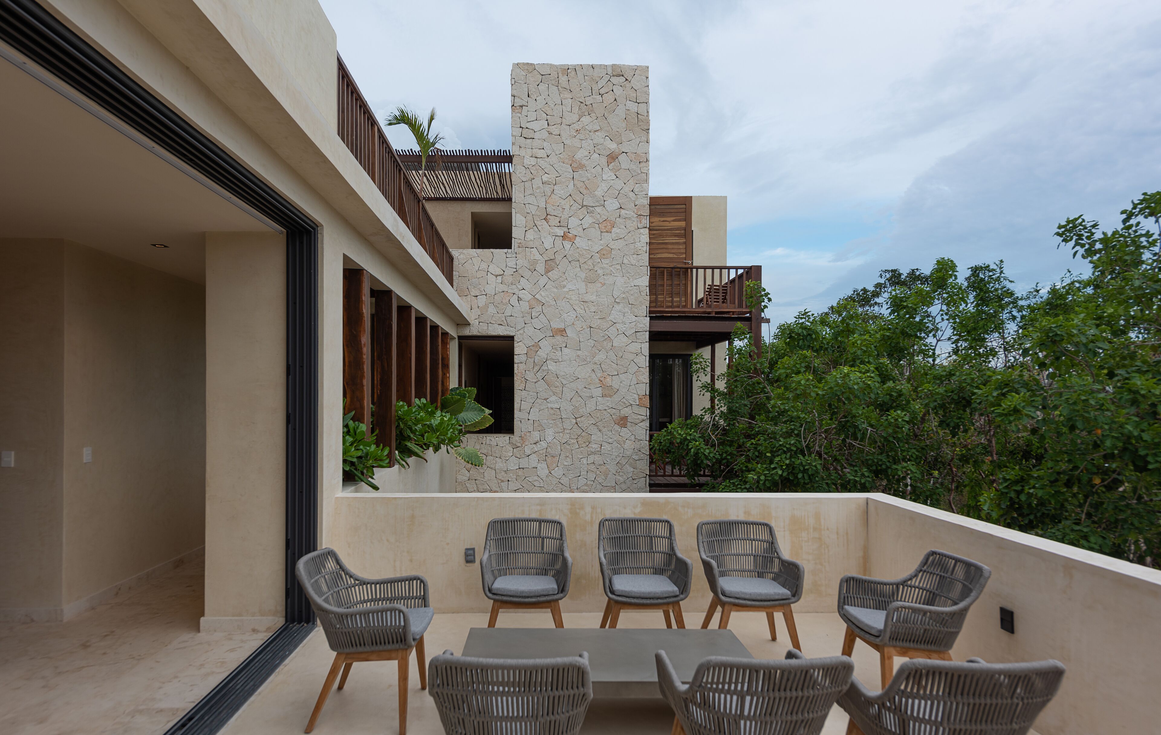 Une terrasse extérieure moderne, agrémentée d’un mur en pierre, de meubles en osier et offrant une vue sur la verdure environnante.