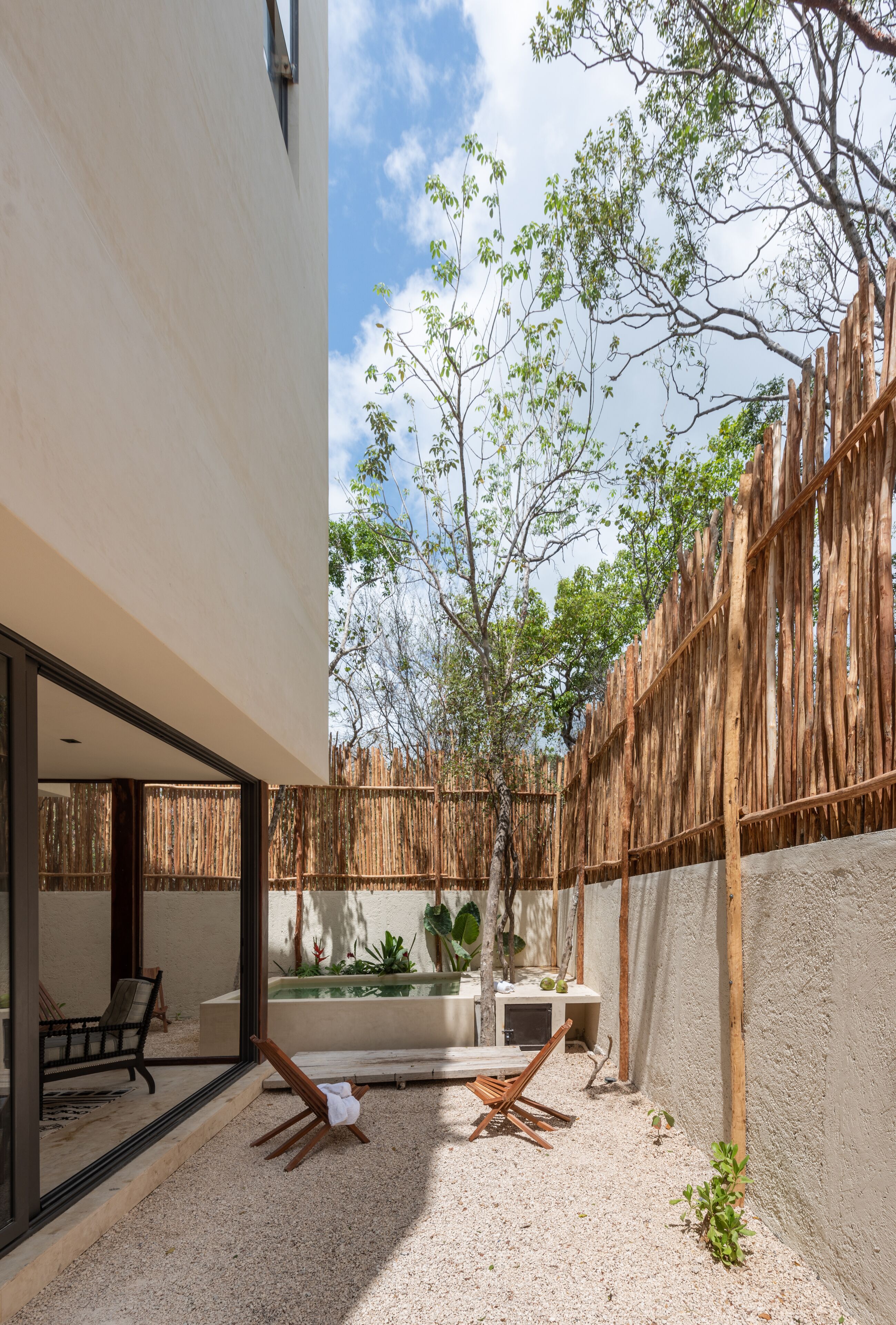 Un patio moderno al aire libre con cerramiento de madera, un área de estar con sillas y una pequeña fuente de agua.
