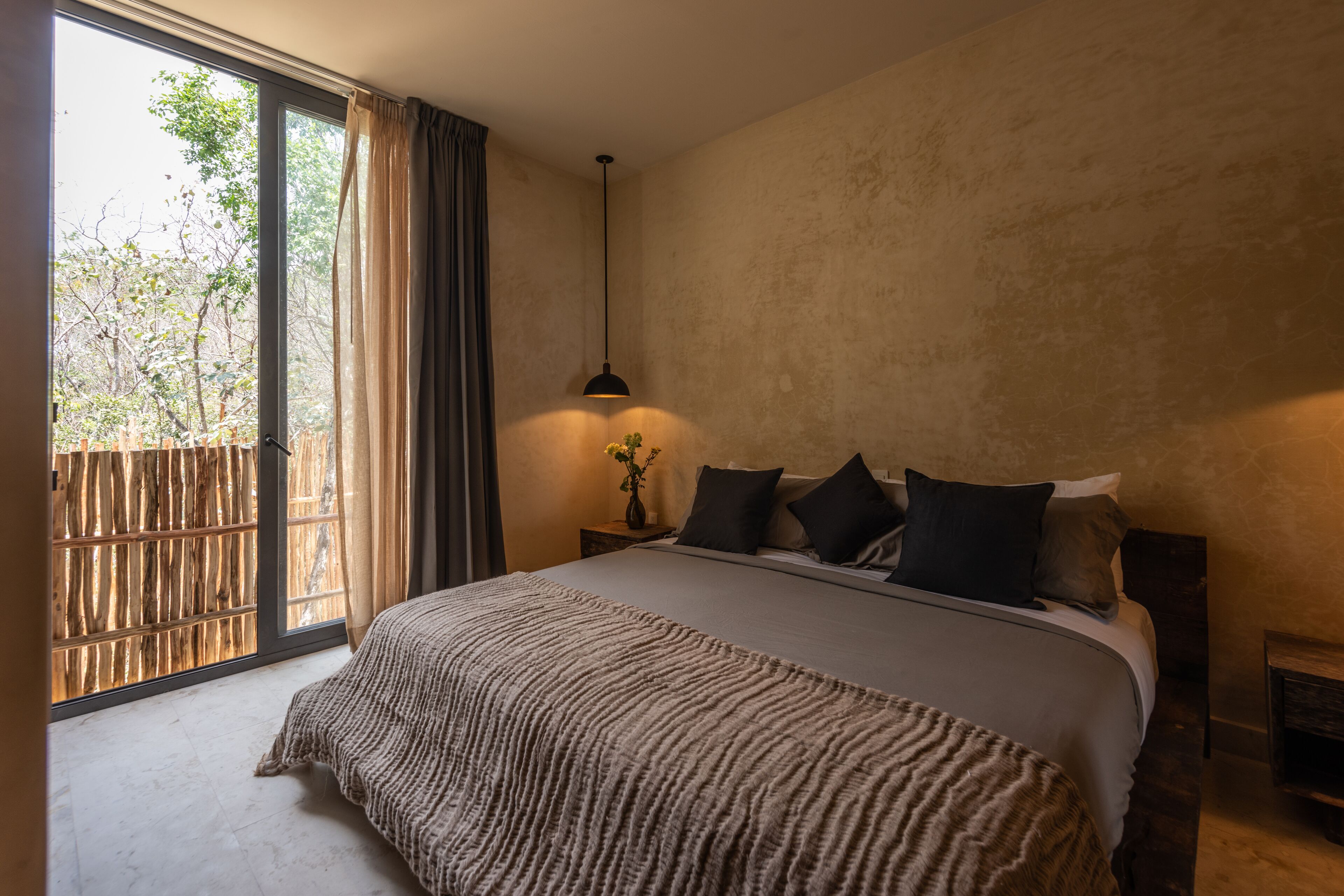 Un dormitorio con una cama grande, una mesita de noche, una lámpara y vistas al exterior a través de una puerta corrediza.