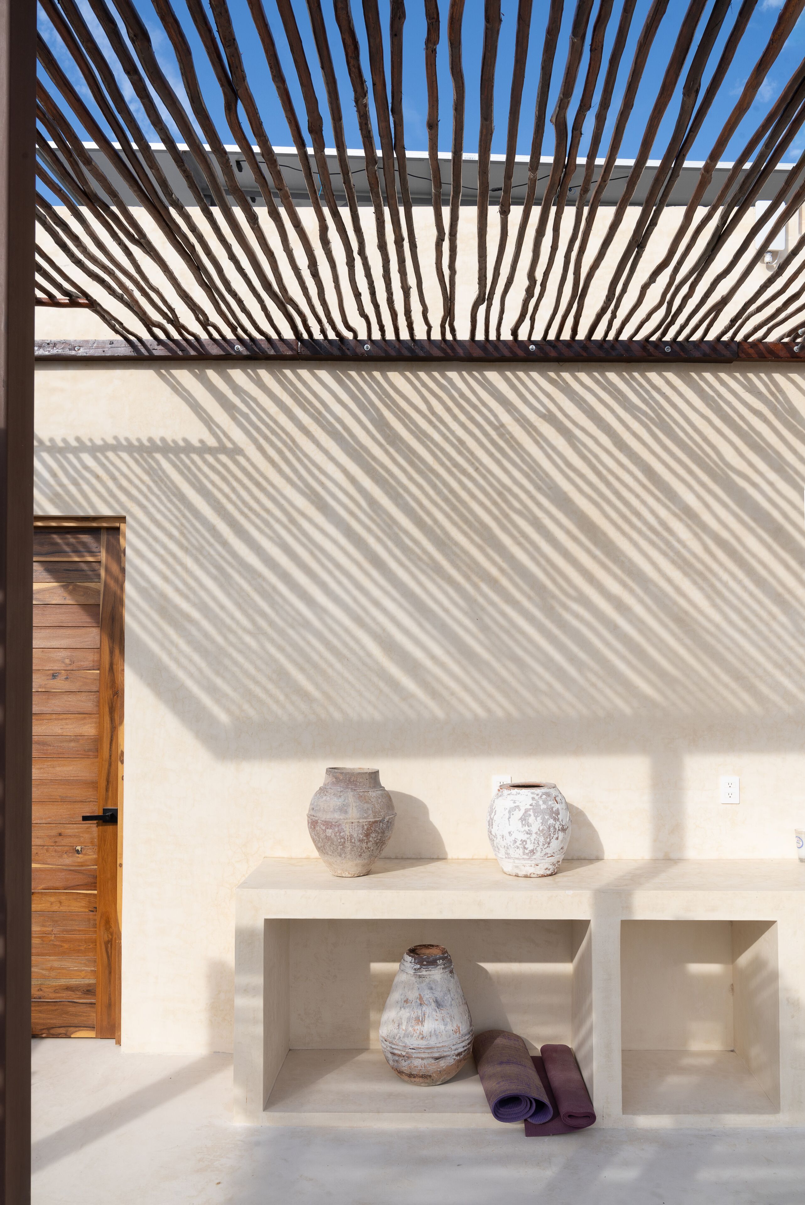 A room with a wooden door, a concrete bench with two pottery pieces, and a yoga mat.